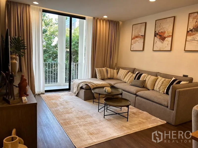Townhouse for rent - Living room with sectional sofa opening to a balcony with greenery.