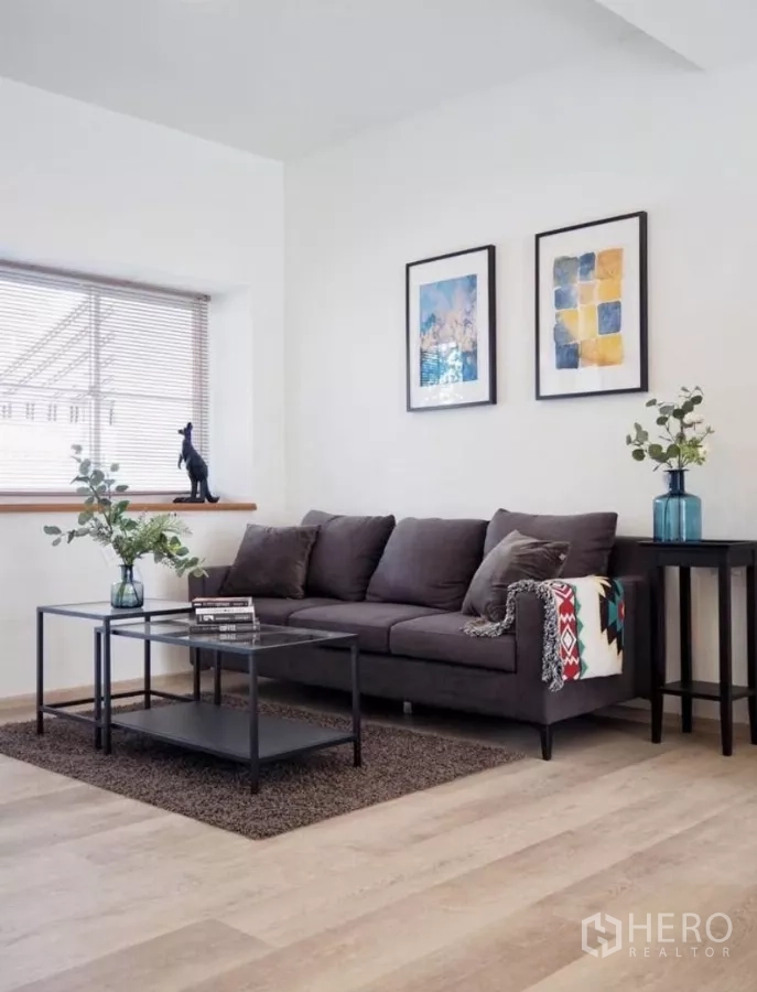 Townhouse for rent in Bang Phli, Samut Prakan - Bright living room with grey sofa, minimalist decor, wood flooring and a wide window with blinds.