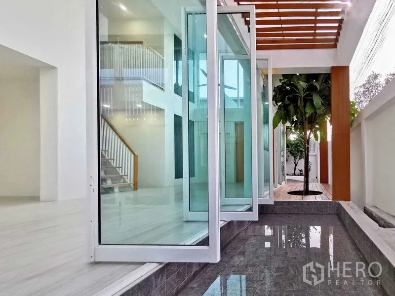 Home Office for sale in Suan Luang, Bangkok - Semi-outdoor corridor with folding glass doors, water feature, and a courtyard tree.