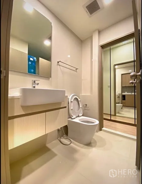 Condominium for sale in Chatuchak, Bangkok - Modern bathroom with large mirror, vanity sink and toilet.