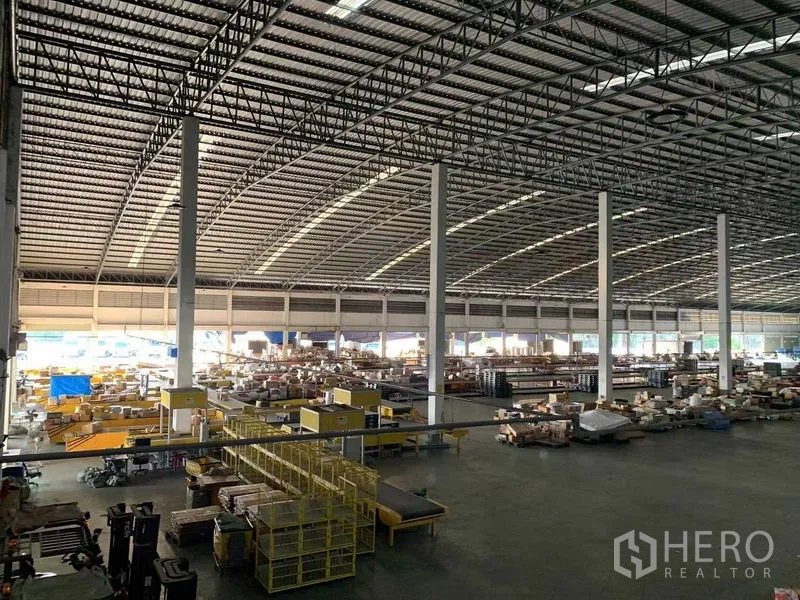Warehouse for rent in Bang Bo, Samut Prakan - Vast warehouse interior with high steel truss roof, tall columns, conveyors and organized storage zones.