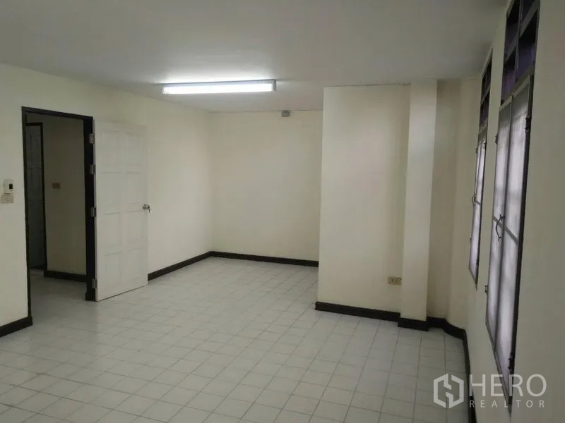 Townhouse for rent in Phra Khanong, Bangkok - Spacious tiled living area with fluorescent ceiling light and a row of windows.