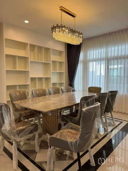 Detached House for rent in Samut Prakan - Dining room with marble table, eight chairs, built-in shelves, and crystal chandelier.