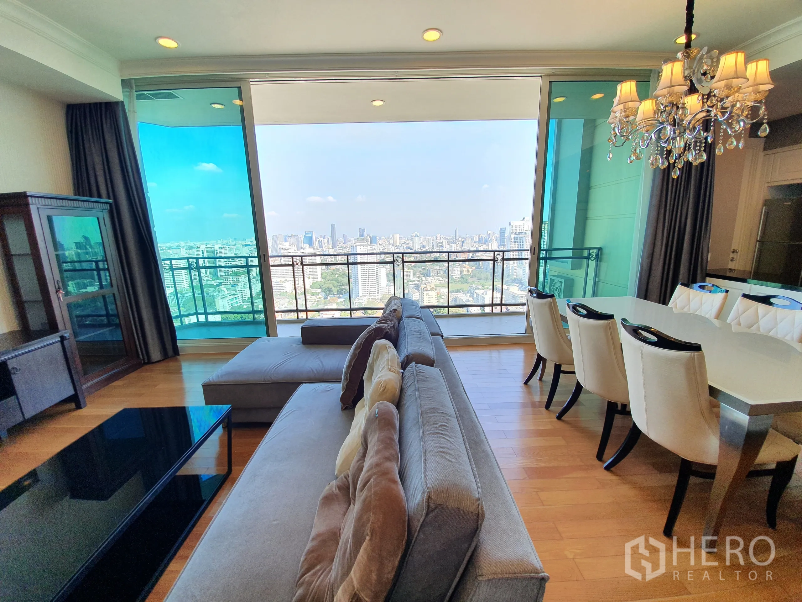 公寓 出租在Watthana, Bangkok - 开放式客厅与六人餐桌，水晶吊灯下，面向宽阔城市景色。