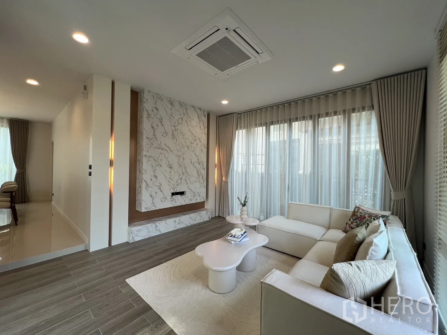 Detached House for rent or sale in Bang Kapi, Bangkok - Bright living room with L-shaped sofa, marble feature wall and sheer curtains.