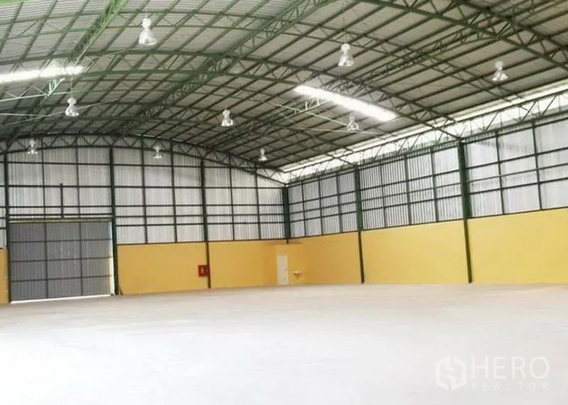 Warehouse for rent in Lat Krabang, Bangkok - Open-plan warehouse floor with bright lighting, wide shutter door and yellow lower walls.