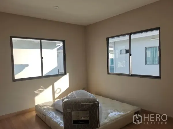 Detached House for sale in Nonthaburi - Bright bedroom with two large windows and a mattress on wood flooring.