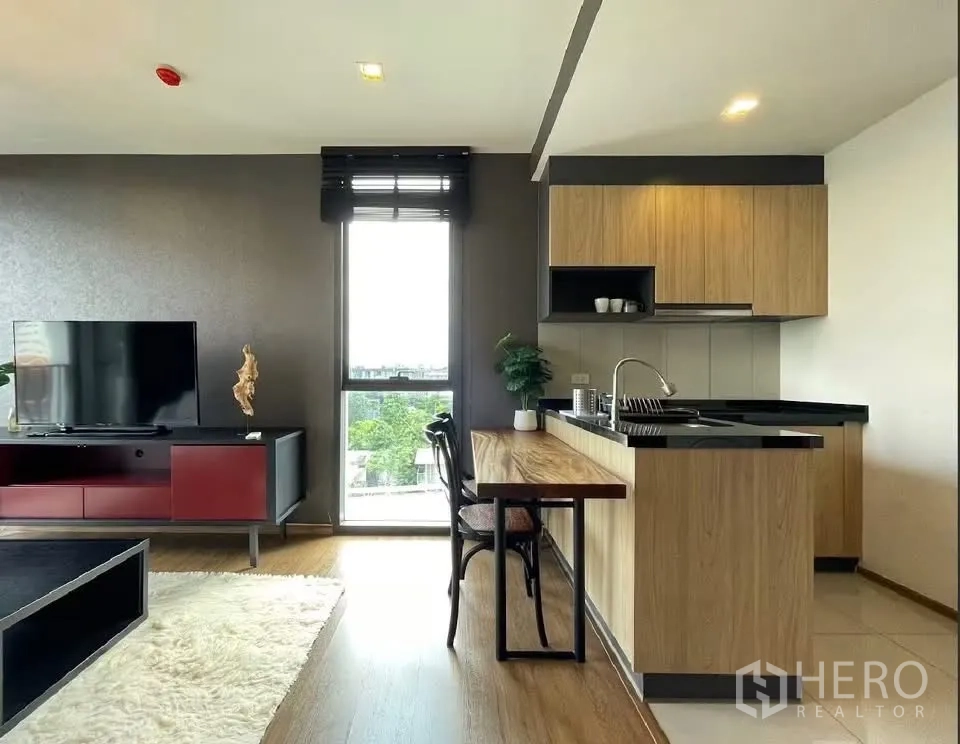 คอนโด for rent in Watthana, Bangkok - พื้นที่นั่งเล่นแบบเปิดโล่งพร้อมชั้นวางทีวี พรม และครัวไม้พร้อมบาร์ทานอาหาร