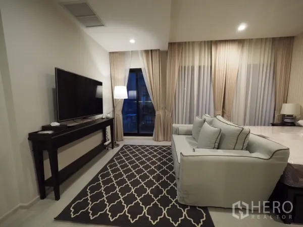 คอนโด ให้เช่าหรือขายในPathum Wan, Bangkok - ห้องนั่งเล่นพร้อมโซฟา ทีวีจอใหญ่ พรมลาย และประตูกระจกออกระเบียงกับผ้าม่านสูง