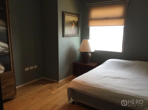 公寓 出租或出售在Watthana, Bangkok - 卧室配木地板与卷帘窗，床头柜与台灯，墙面装饰画及内置柜。