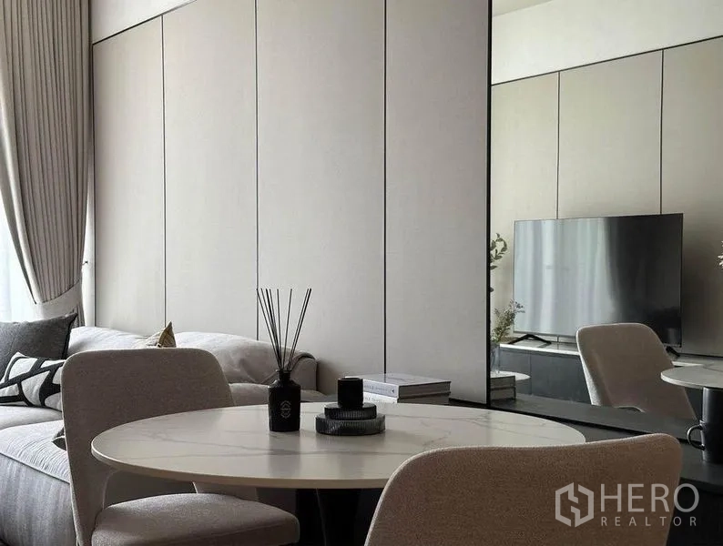 Condominium for rent in Watthana, Bangkok - Two-seat round dining table facing a mirrored wall with reflections of the TV and sofa, full-height curtains nearby.
