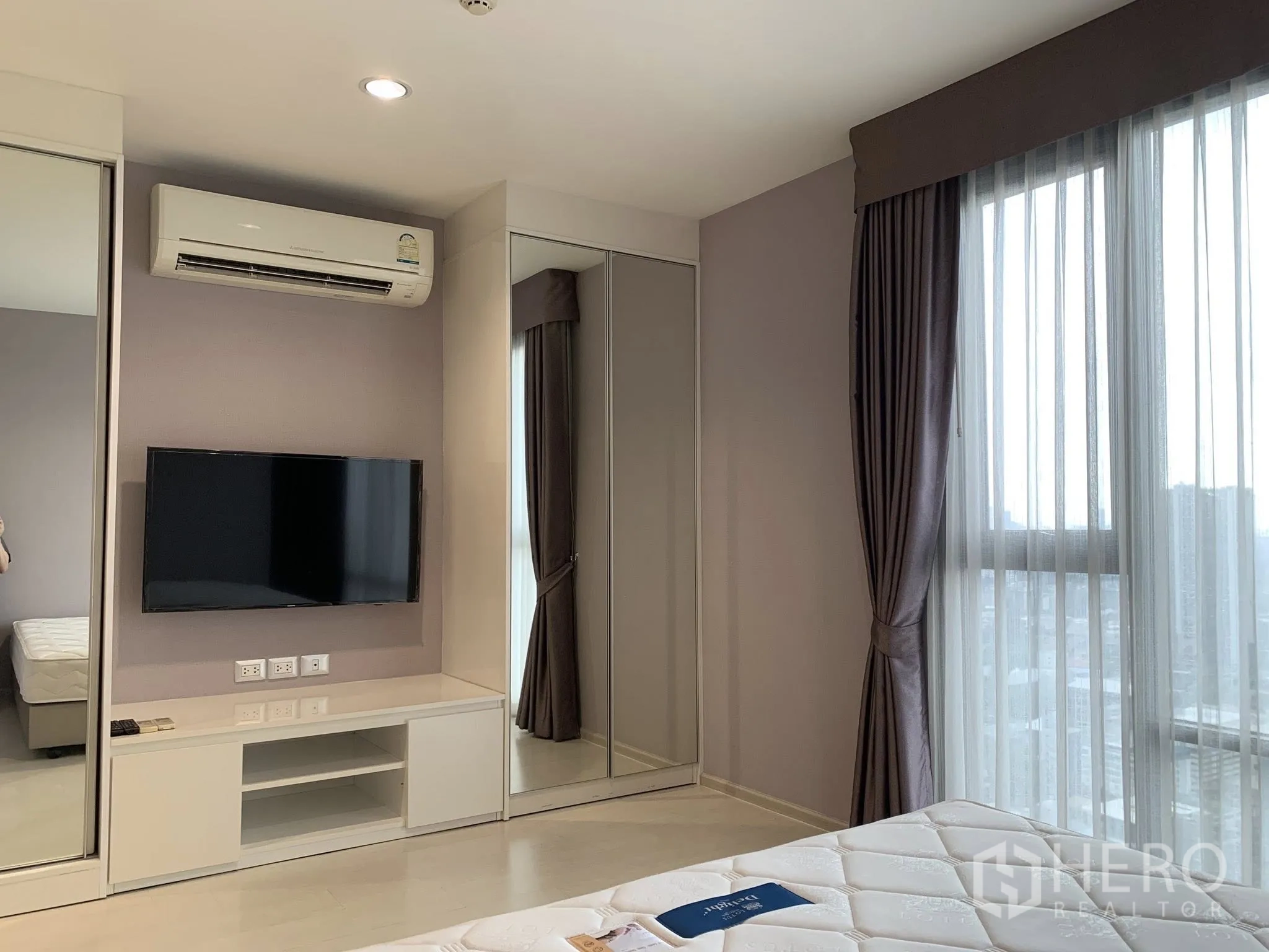 Condominium for rent in Khlong Toei, Bangkok - Bedroom with mirrored wardrobes, TV unit, air conditioner, and full-length curtains.
