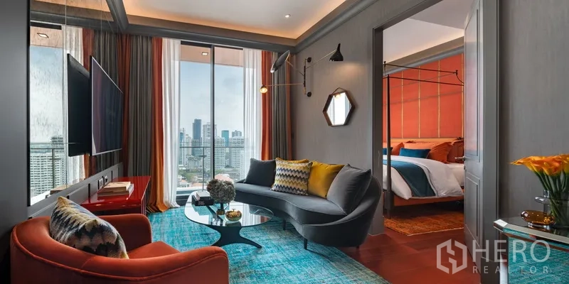 Condominium for sale in Watthana, Bangkok - Modern living room with a curved sofa, floor‑to‑ceiling windows, and a glimpse of the bedroom.