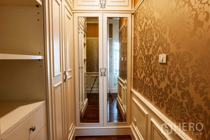 Condominium for rent in Watthana, Bangkok - Walk-in closet corridor with mirrored wardrobe doors, built-in storage and gold damask wallpaper.