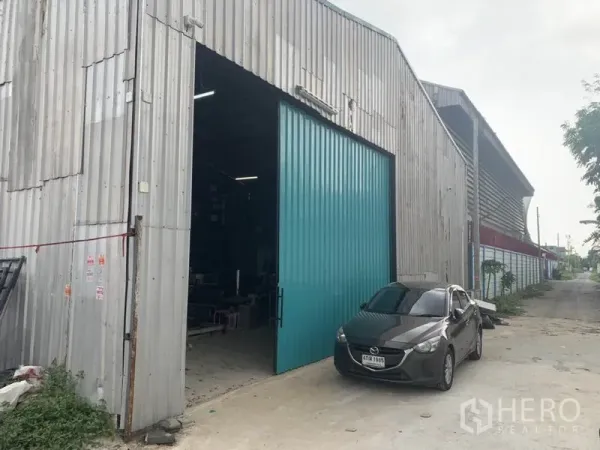 货栈 出租在Bang Kapi, Bangkok - 金属外墙仓库外观，宽大的青色推拉门与车道停车位，位于Bang Kapi。