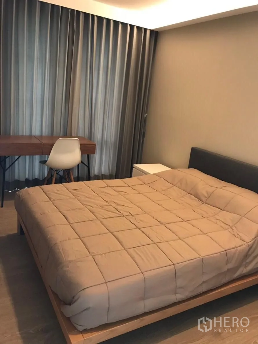 Condominium for rent in Watthana, Bangkok - Primary bedroom with padded headboard, full curtains, wooden desk and chair.