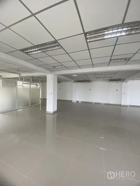 Office Space for rent in Khlong Toei, Bangkok - Open-plan office with grid ceiling, fluorescent lighting, glossy tile floors, columns and glass partitions.