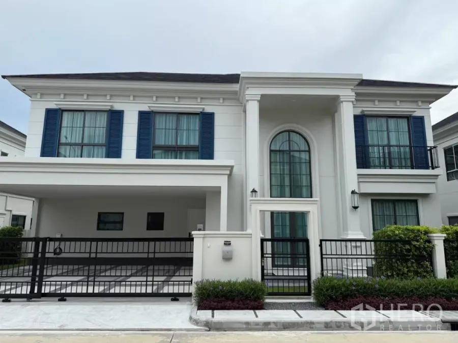 独立式住宅 出租或出售在Bang Phli, Samut Prakan - 两层现代经典风格的别墅外观，蓝色百叶窗、拱形门廊与带门车棚。