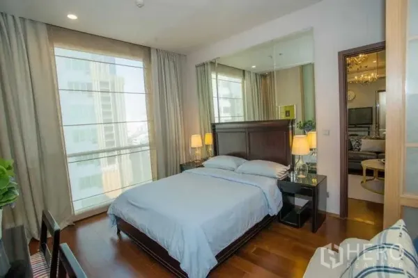 Condominium for rent in Watthana, Bangkok - Sunlit bedroom with large windows, wooden flooring, dark wood bed and mirrored headboard wall.