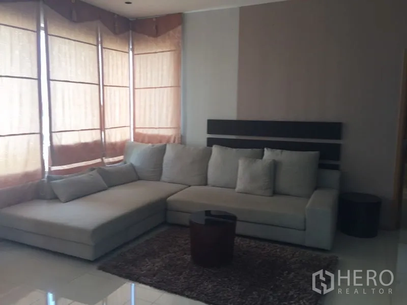 คอนโด ให้เช่า - มุมนั่งเล่นสบายพร้อมโซฟาตัวแอล พรม และหน้าต่างบานยาวมีม่านพับ