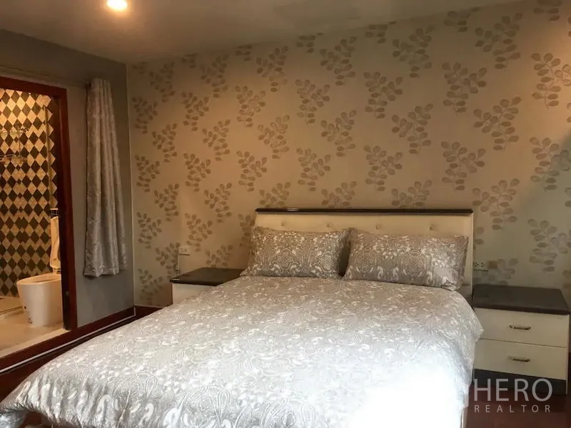 ทาวน์เฮาส์ ให้เช่าในBang Rak, Bangkok - ห้องนอนวอลเปเปอร์ลายใบไม้ เตียงควีน โต๊ะข้างเตียง และทางเข้าห้องน้ำในตัว