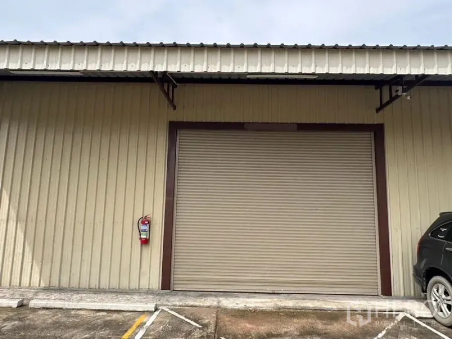 Warehouse for rent in Mueang Nonthaburi, Nonthaburi - Close view of closed rolling shutter on metal-clad warehouse with parking area in front.