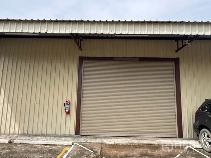 Warehouse for rent in Mueang Nonthaburi, Nonthaburi - Close view of closed rolling shutter on metal-clad warehouse with parking area in front.