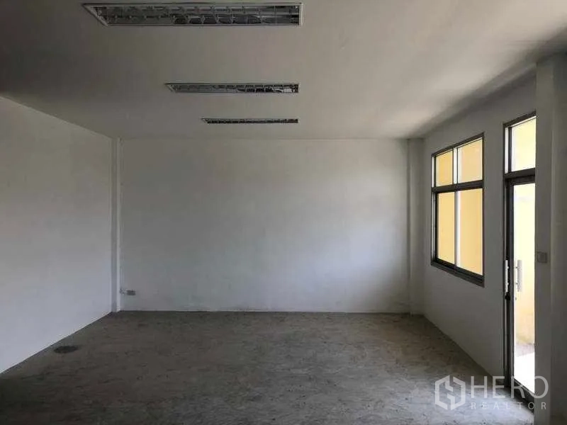 Factory for rent in Khlong Luang, Pathum Thani - Bright upstairs office room with multiple windows and a door opening to a corridor.