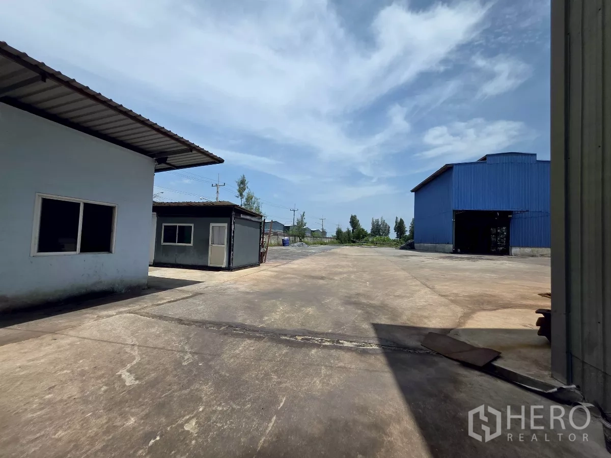 Factory for rent in Mueang Samut Sakhon, Samut Sakhon - Expansive concrete yard for truck maneuvering between service buildings and a blue warehouse.