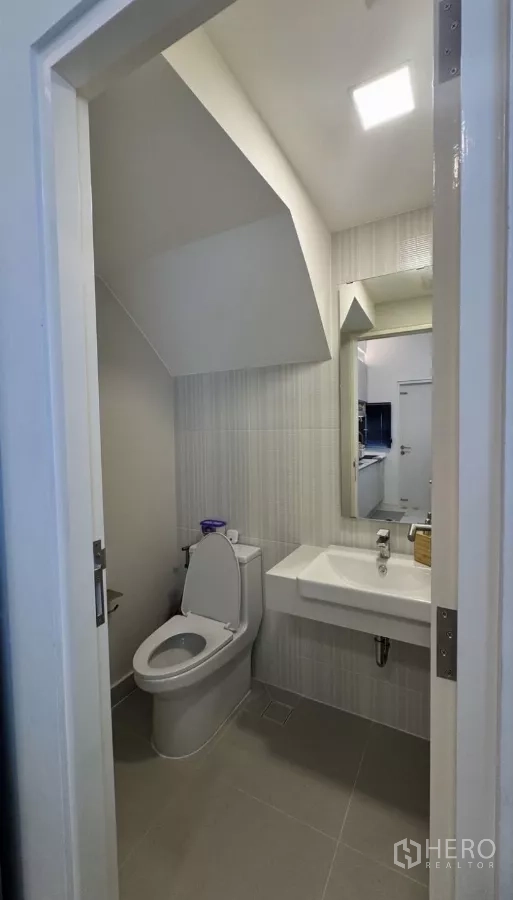Townhouse for rent in Bang Phli, Samut Prakan - Clean bathroom under the stairs with toilet, wall mirror and rectangular sink.