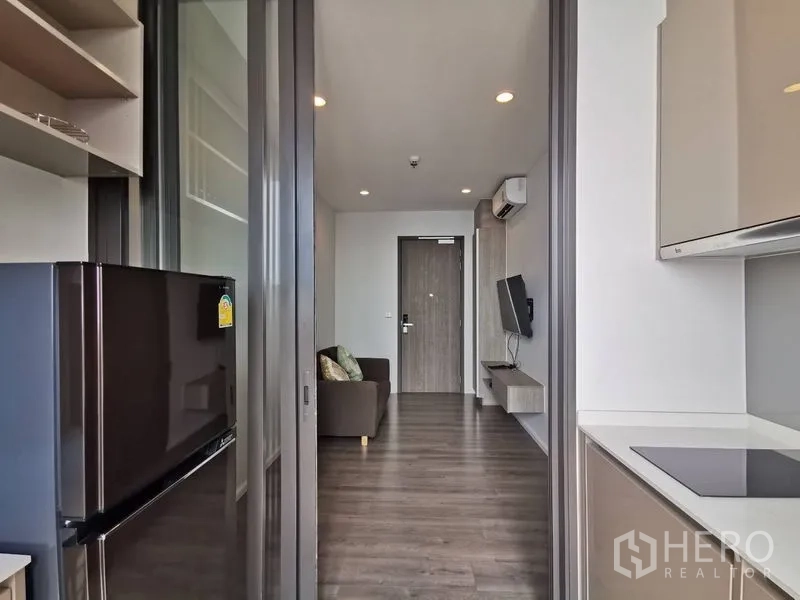 公寓 出售在Phra Khanong, Bangkok - 滑动玻璃隔断后的紧凑厨房，带炉灶与冰箱，连接客厅。