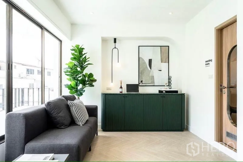 Office Space for rent in Khlong Toei, Bangkok - Reception lounge with dark sofa, floor-to-ceiling windows, green front desk, pendant light and contemporary artwork.