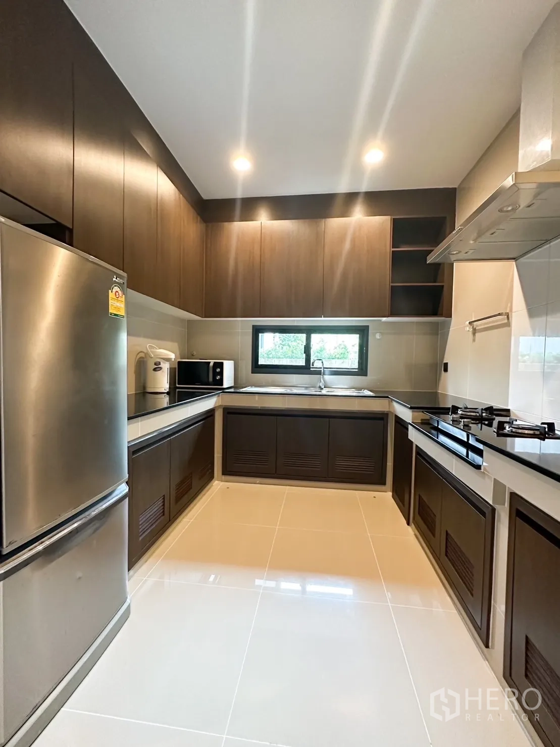 Detached House for rent or sale in Bang Kapi, Bangkok - U-shaped kitchen with dark wood cabinets, gas hob and stainless refrigerator.