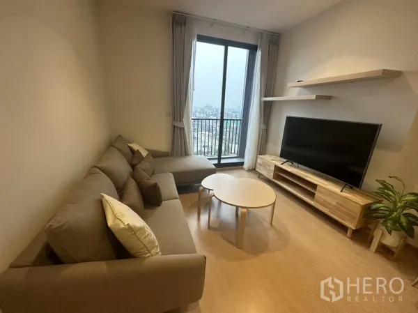 公寓 出租在Watthana, Bangkok - 采光良好的客厅，L形沙发、电视柜与通往阳台的城市景观