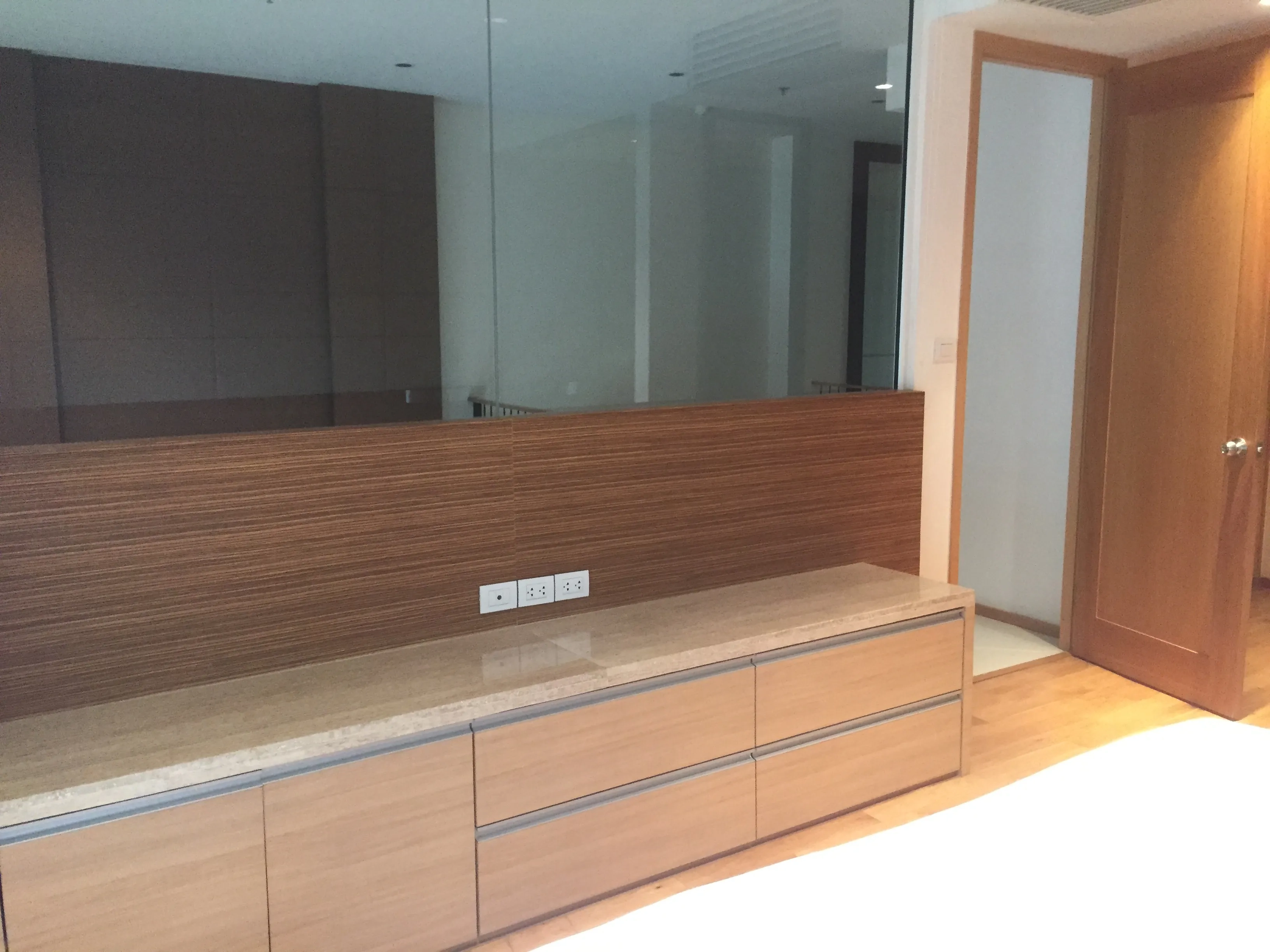 Condominium for rent in Sathon, Bangkok - Bedroom corner featuring built-in wood cabinetry and a mirrored wall near the ensuite door.