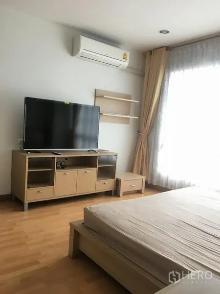 Condominium for rent in Khlong Toei, Bangkok - Bright bedroom with double bed, TV cabinet, wall air-conditioner and large window with curtains.