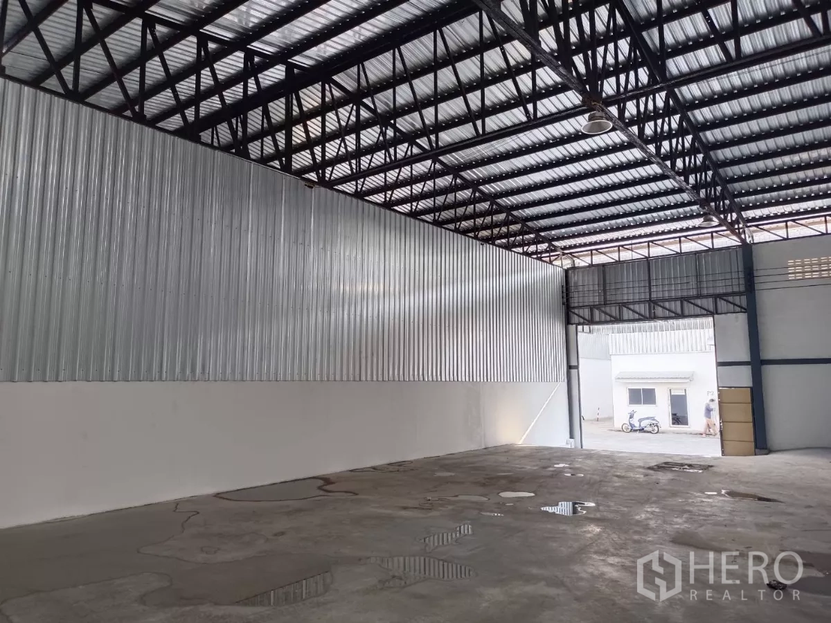 Warehouse for rent in Suan Luang, Bangkok - Open warehouse floor with metal-clad wall and tall roller shutter opening to the yard.