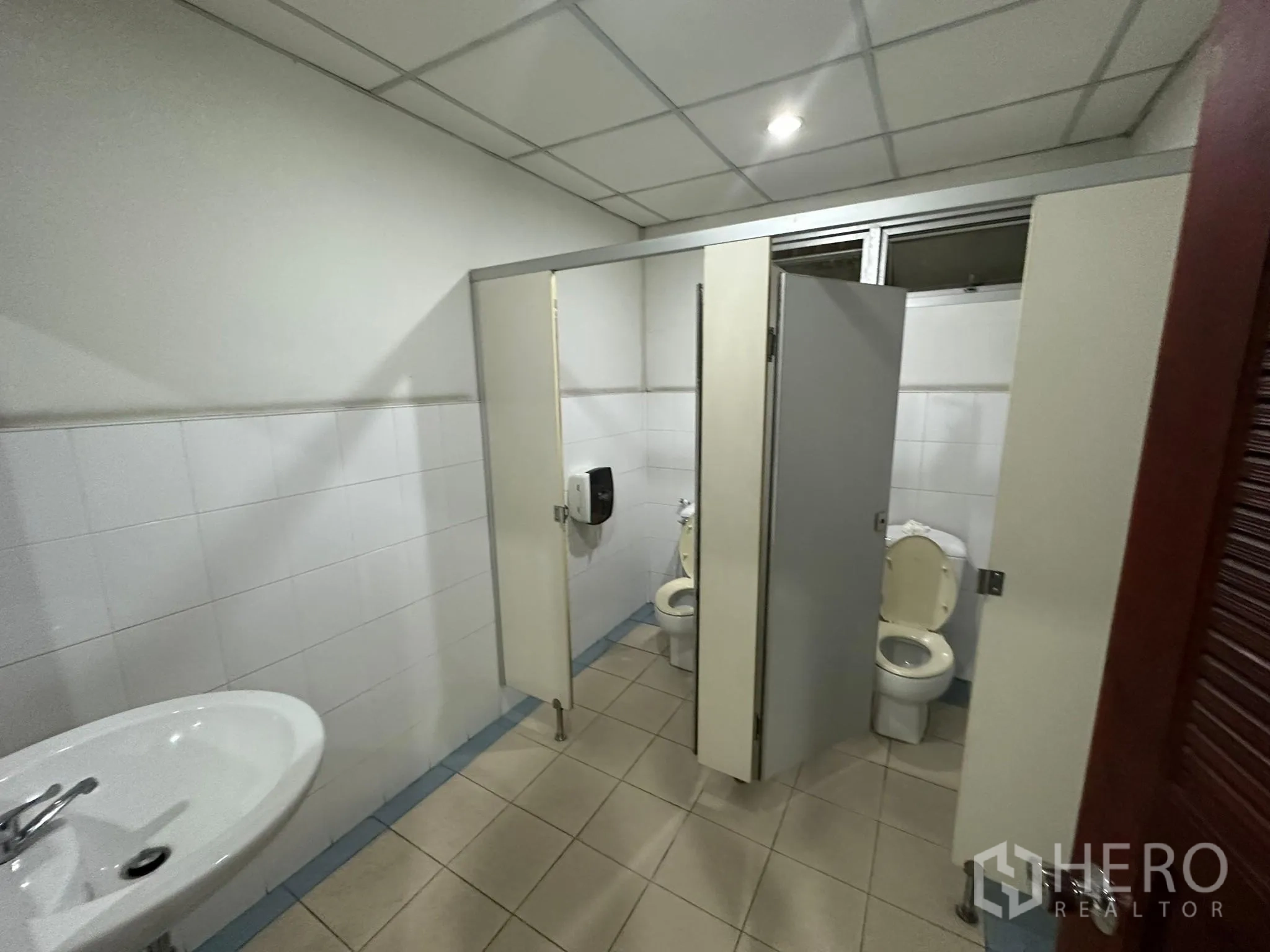 Warehouse for rent in Huai Khwang, Bangkok - Restroom with two toilet stalls, sink and tiled walls.