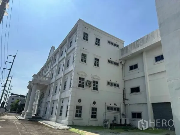 โรงงาน ให้เช่าหรือขายในThanyaburi, Pathum Thani - อาคารสำนักงานโรงงานสีขาวสูงสี่ชั้น มีเสาคลาสสิกและทางขนถ่ายด้านข้าง ใต้ท้องฟ้าโปร่ง