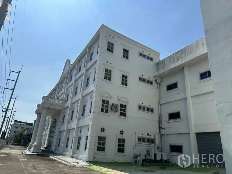 โรงงาน ให้เช่าหรือขายในThanyaburi, Pathum Thani - อาคารสำนักงานโรงงานสีขาวสูงสี่ชั้น มีเสาคลาสสิกและทางขนถ่ายด้านข้าง ใต้ท้องฟ้าโปร่ง