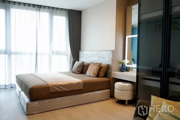 Condominium for rent in Watthana, Bangkok - Master bedroom with large bed, sheer curtains, vanity with lighted mirror and built‑in wardrobe.