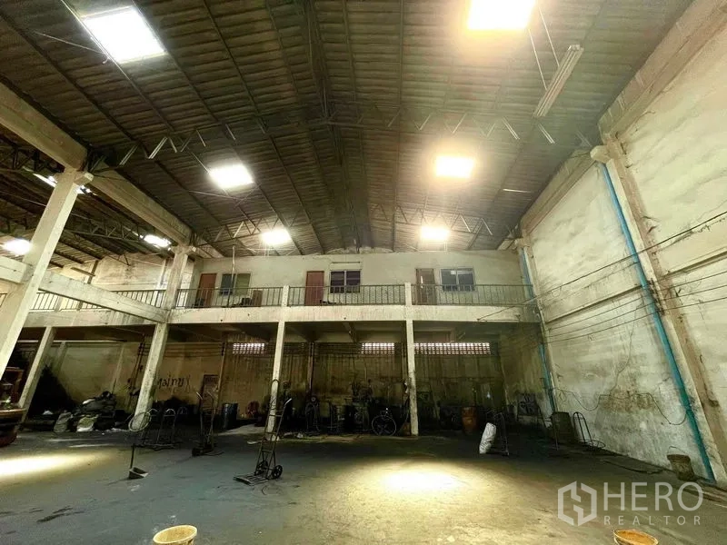 Warehouse for rent in Krathum Baen, Samut Sakhon - Spacious high‑ceiling warehouse interior with mezzanine level, concrete columns and bright industrial lighting.