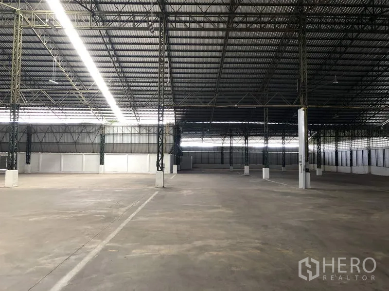 货栈 出租在Mueang Pathum Thani, Pathum Thani - 空置仓库大厅，标示行车通道，高挑屋顶与侧墙通风板保障空气流通。