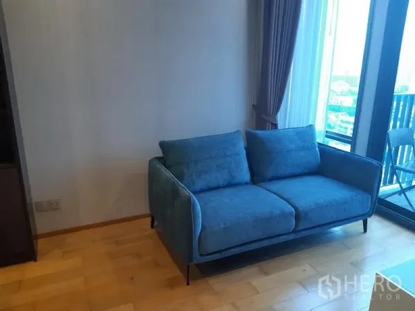 Condominium for rent in Khlong Toei, Bangkok - Cozy living corner with blue sofa beside floor-to-ceiling balcony doors.