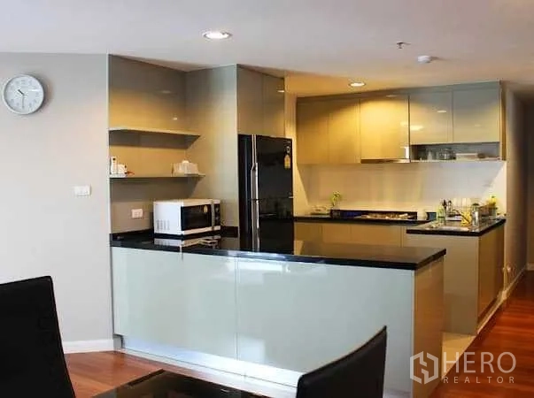 Condominium for rent in Huai Khwang, Bangkok - U-shaped modern kitchen with glossy cabinets, black stone countertops, refrigerator and microwave.