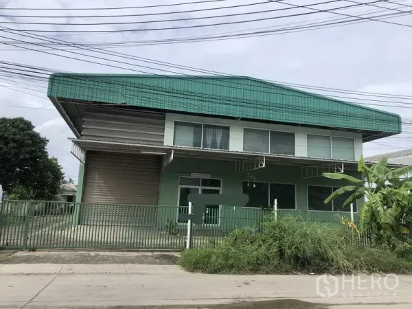 工厂 出租或出售在Samut Prakan - 两层办公楼配仓库的正立面，带绿色围栏和大型卷闸门。