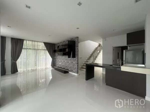 Detached House for sale in Bang Kapi, Bangkok - Bright living space with floor-to-ceiling curtains, glass-railed staircase, and kitchen island.