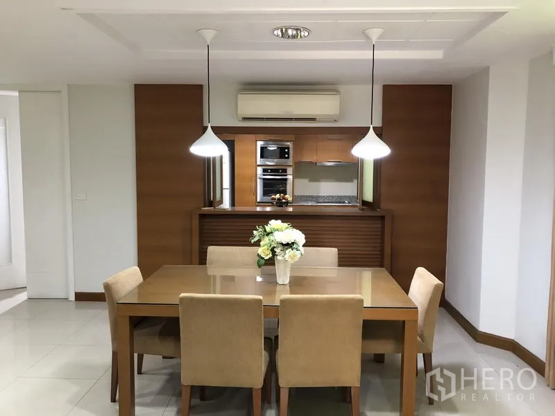 Detached House for rent in Watthana, Bangkok - Dining area with pendant lights and a six-seat table facing a wood-finished kitchen.