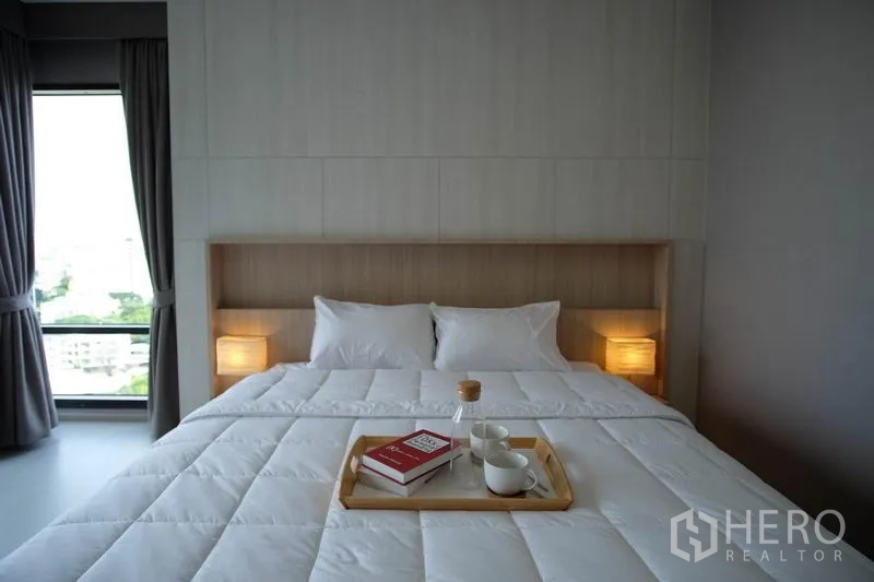 Condominium for rent in Khlong Toei, Bangkok - Master bedroom with padded headboard, warm bedside lighting and tray on the bed.