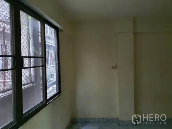Shophouse for rent in Bang Rak, Bangkok - Small corner room with metal-framed window and security mesh providing natural light.